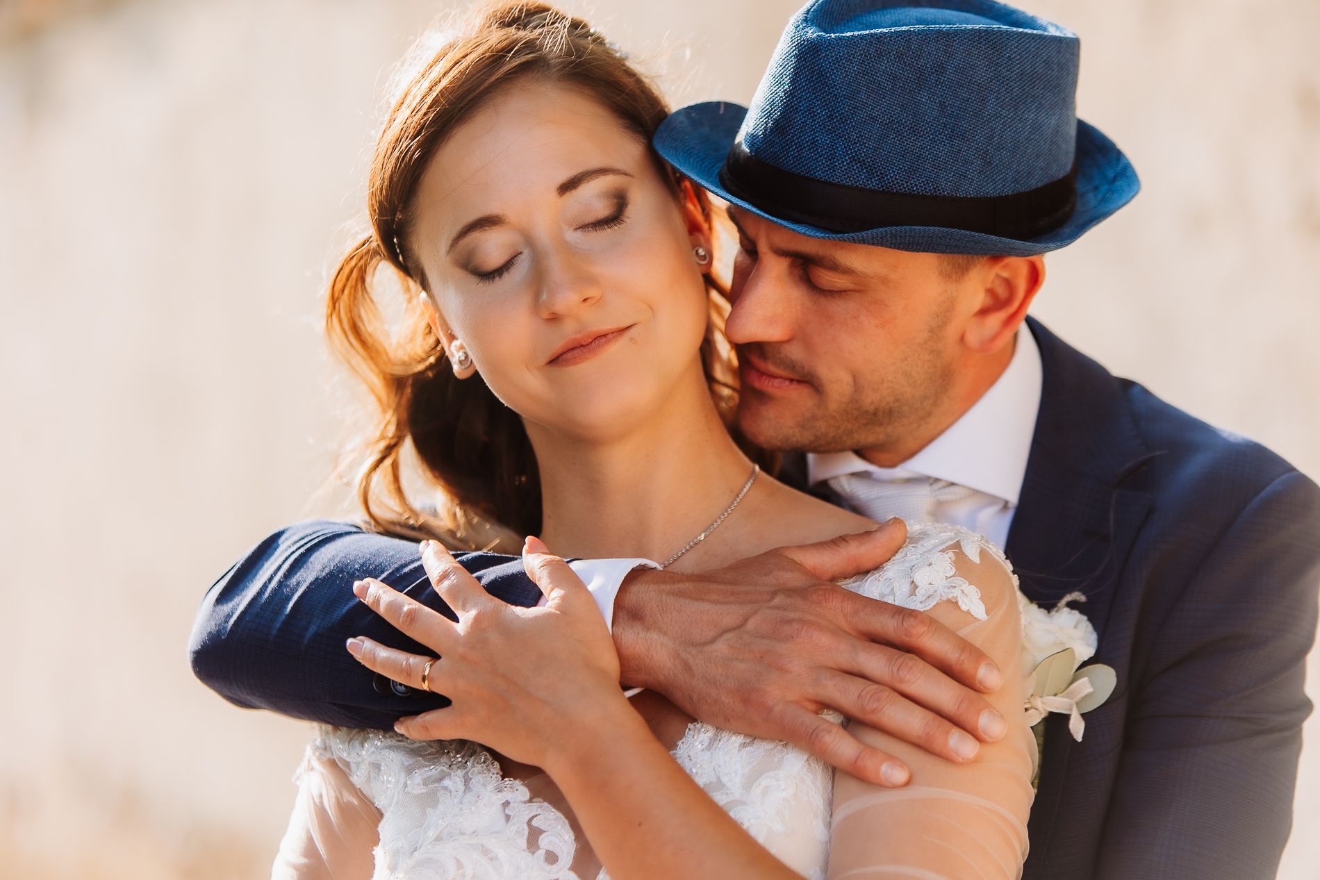 A wedding couple embraces tenderly in golden light while wearing formal blue suit and white dress.