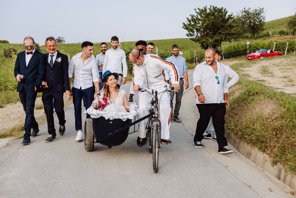 Wedding party walks together down a rural path with one person using a wheelchair on a sunny day.