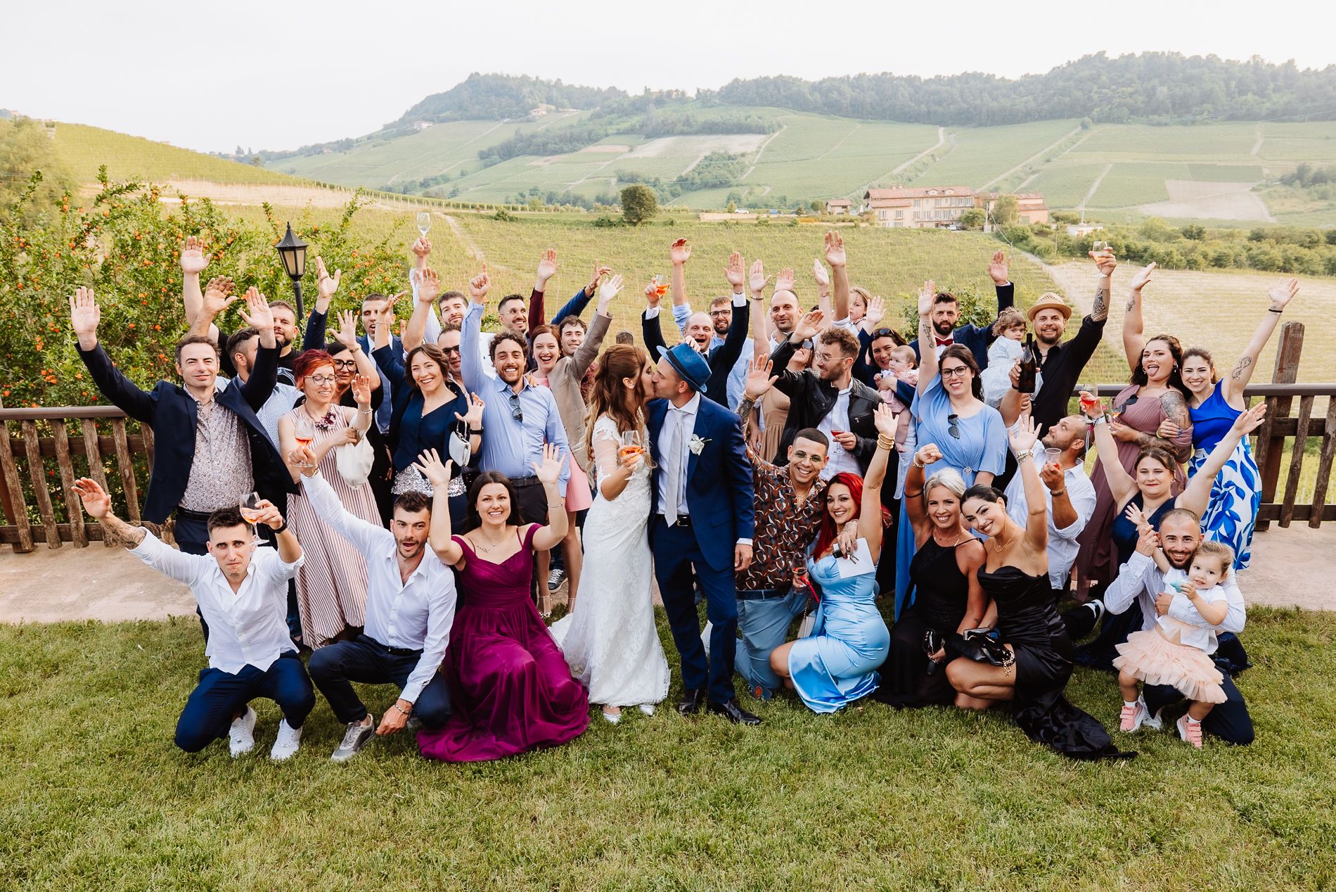 Wedding party celebrating on a grassy hillside with mountains in the background during sunset.