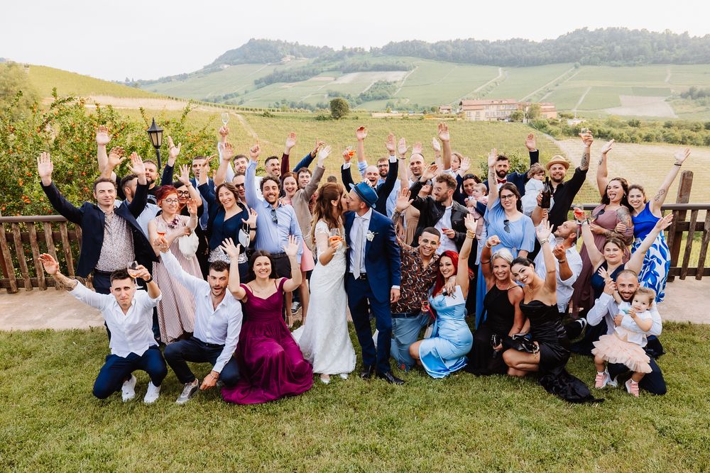 Wedding party celebrating on a grassy hillside with mountains in the background during sunset.