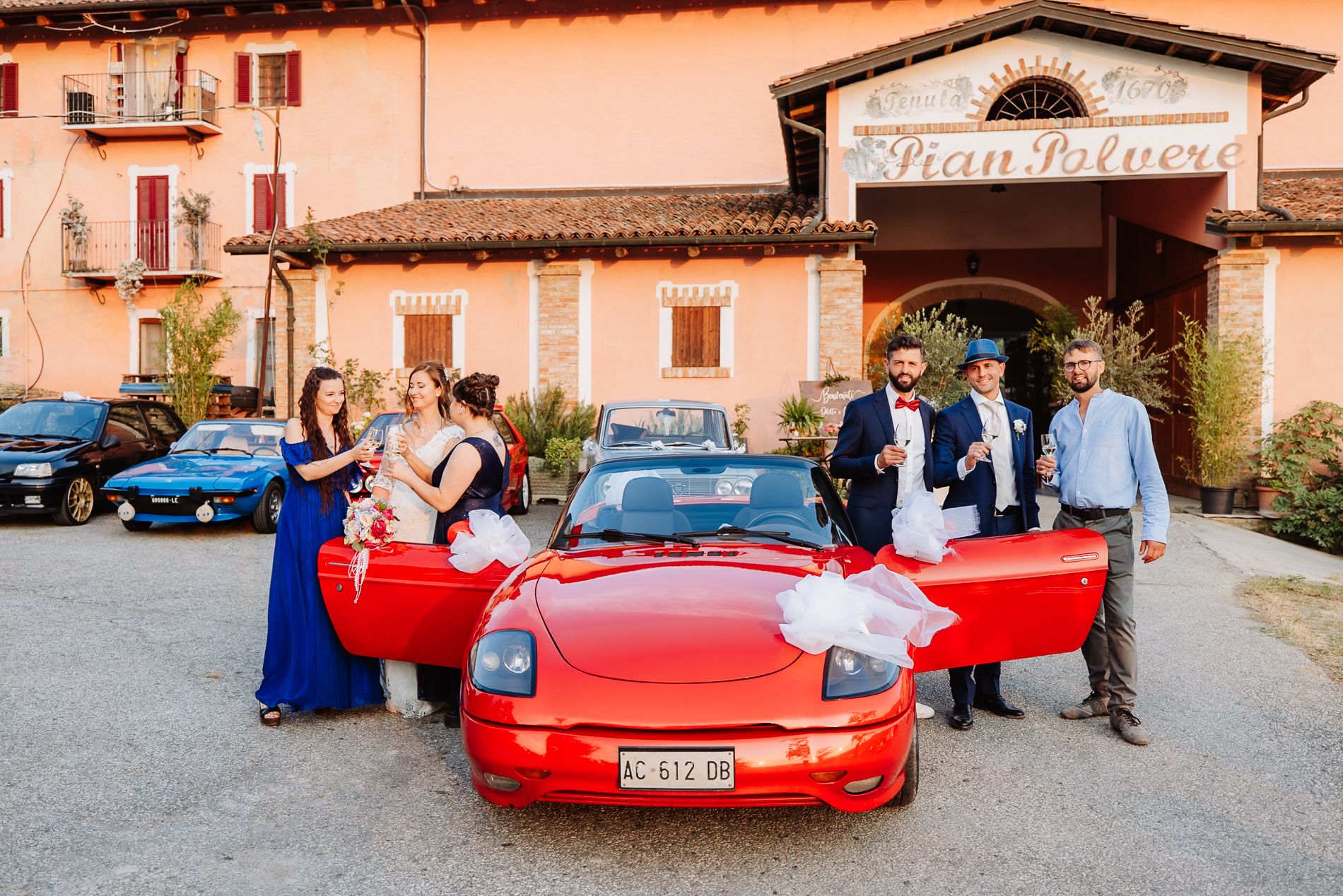 A red Ferrari drives along scenic roads near rustic Italian buildings and stone walls.