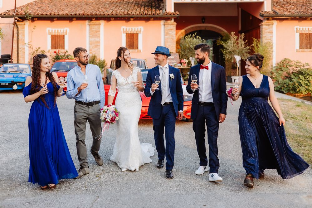 A wedding party walks together laughing and smiling outside a rustic Italian villa with blue and white formal attire.