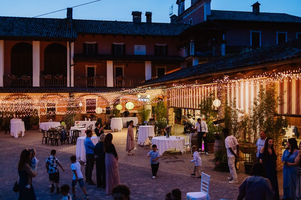An outdoor evening wedding reception with string lights decorating a terrace area where guests mingle around tables.