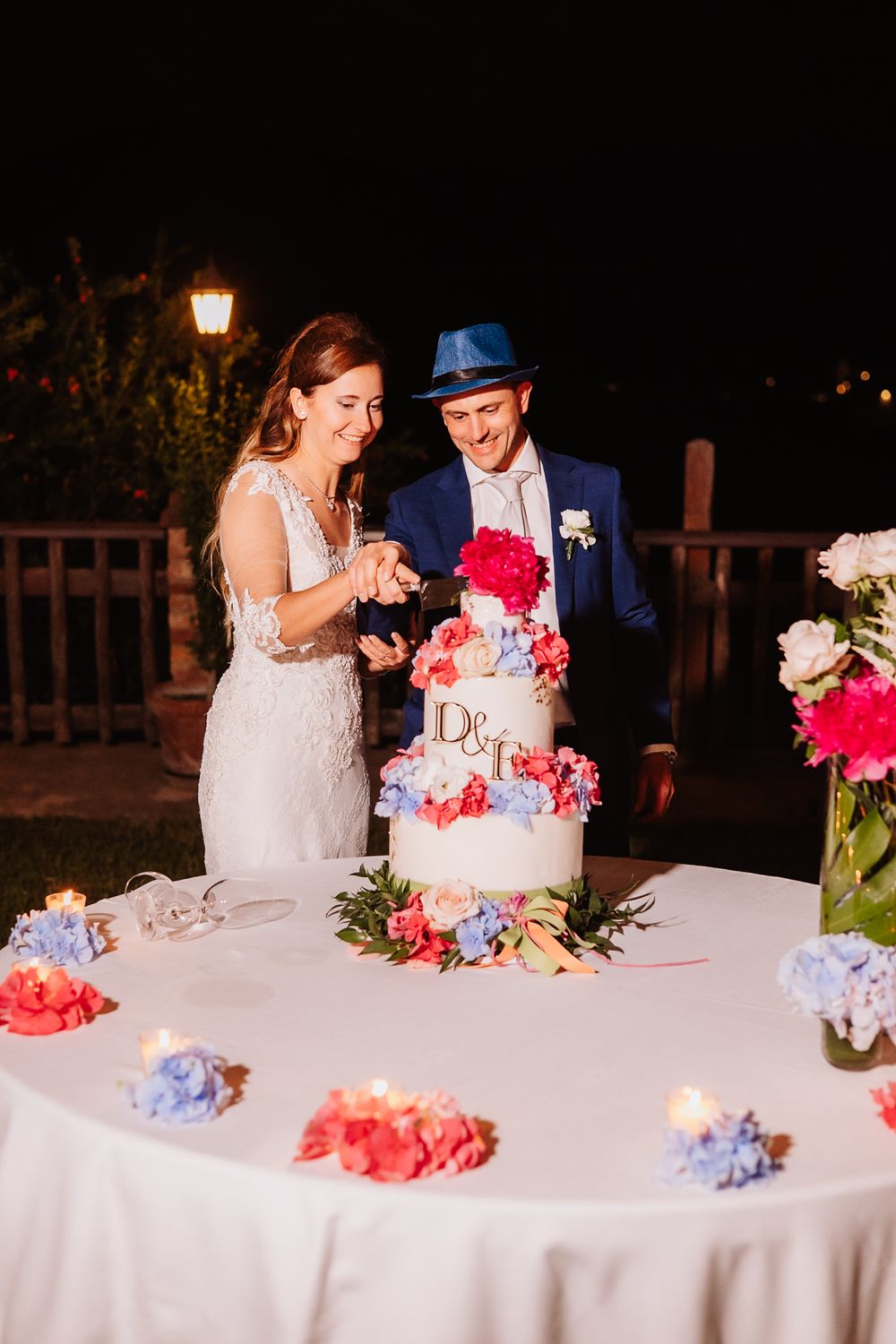 A couple sharing a moment while cutting their wedding cake decorated with pink and blue flowers on a white tablecloth.