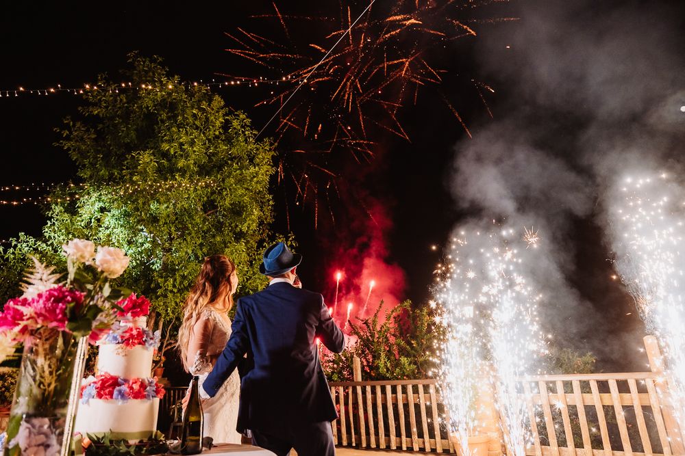 Sparkling firework fountains illuminate an outdoor celebration at night with people gathered beneath the colorful pyrotechnics.