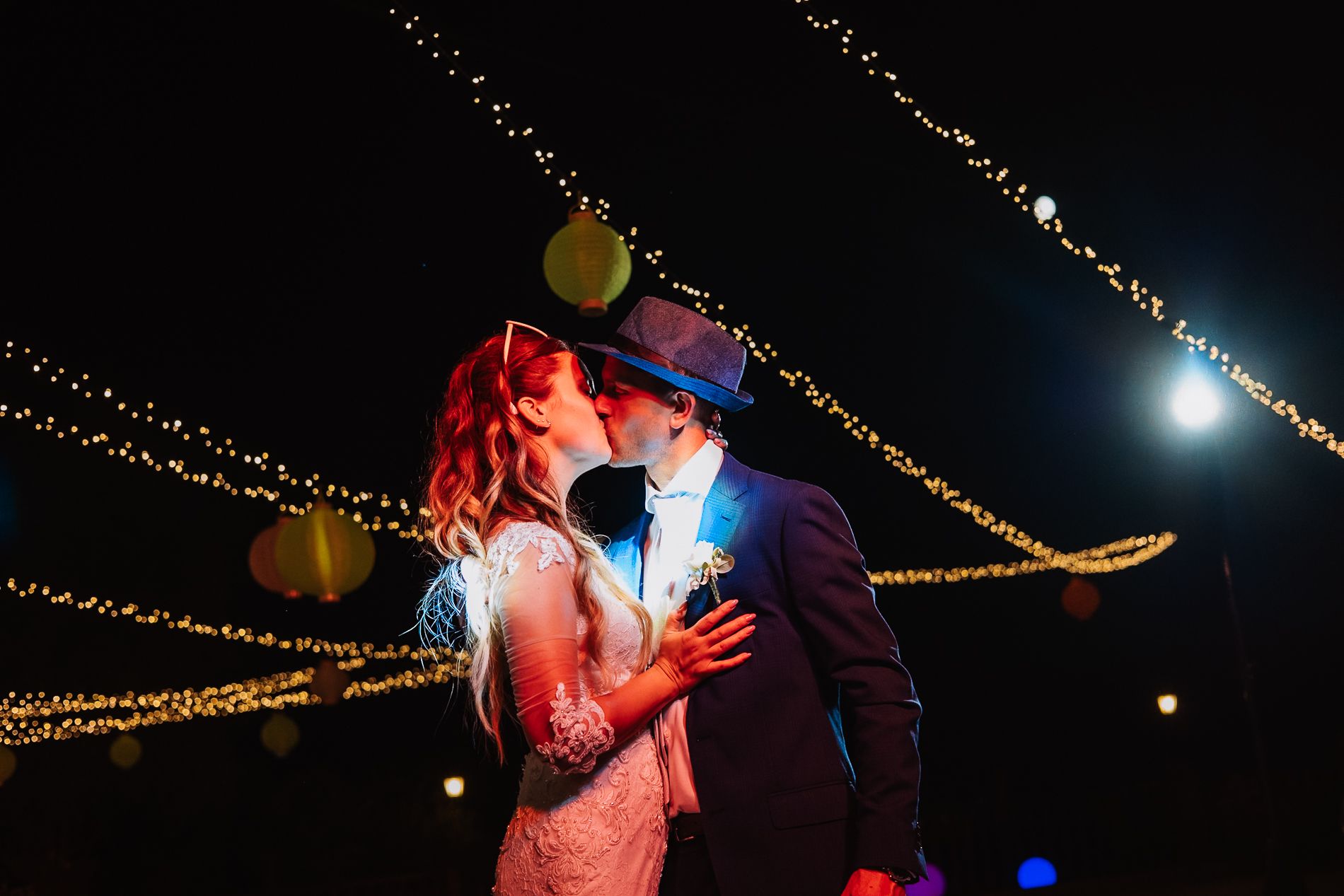 A romantic couple dances beneath twinkling string lights at an outdoor evening celebration.