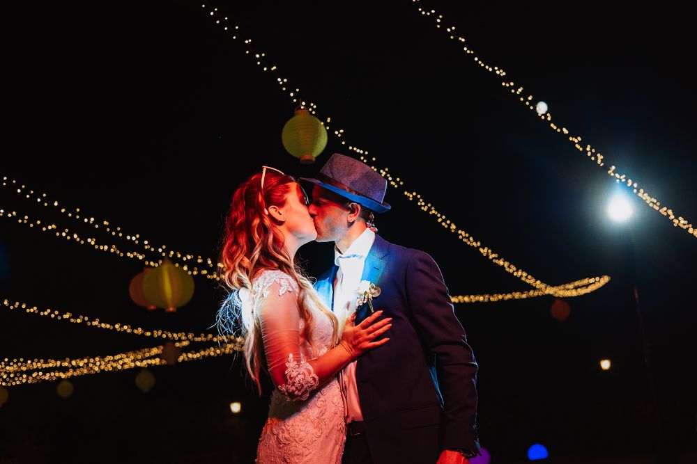 A romantic couple dances beneath twinkling string lights at an outdoor evening celebration.