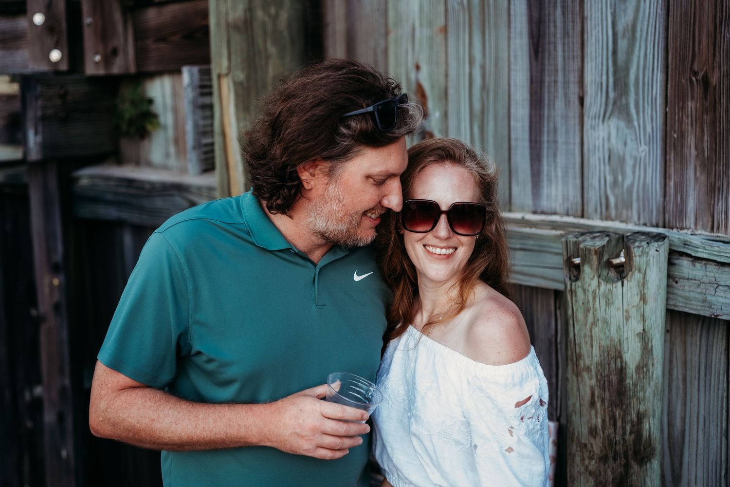 Trent, wearing a teal shirt, looks down at Stacy wearing sunglasses and a white off-the-shoulder shirt.