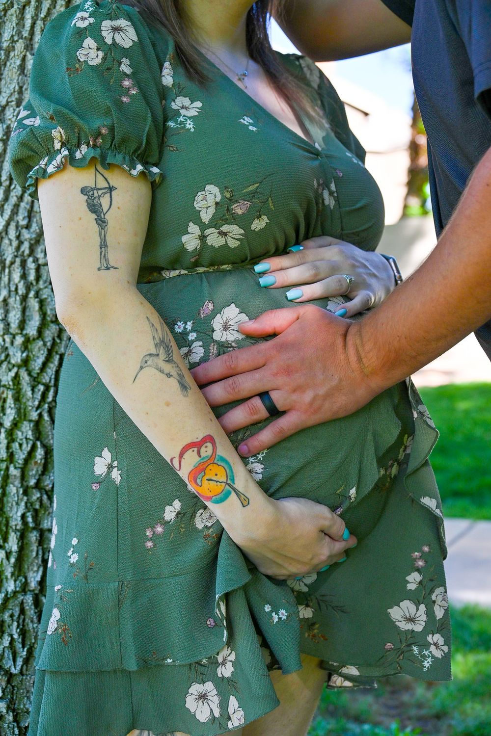 Close-up of tattooed pregnant woman's baby bump with partner's hand resting gently on belly.