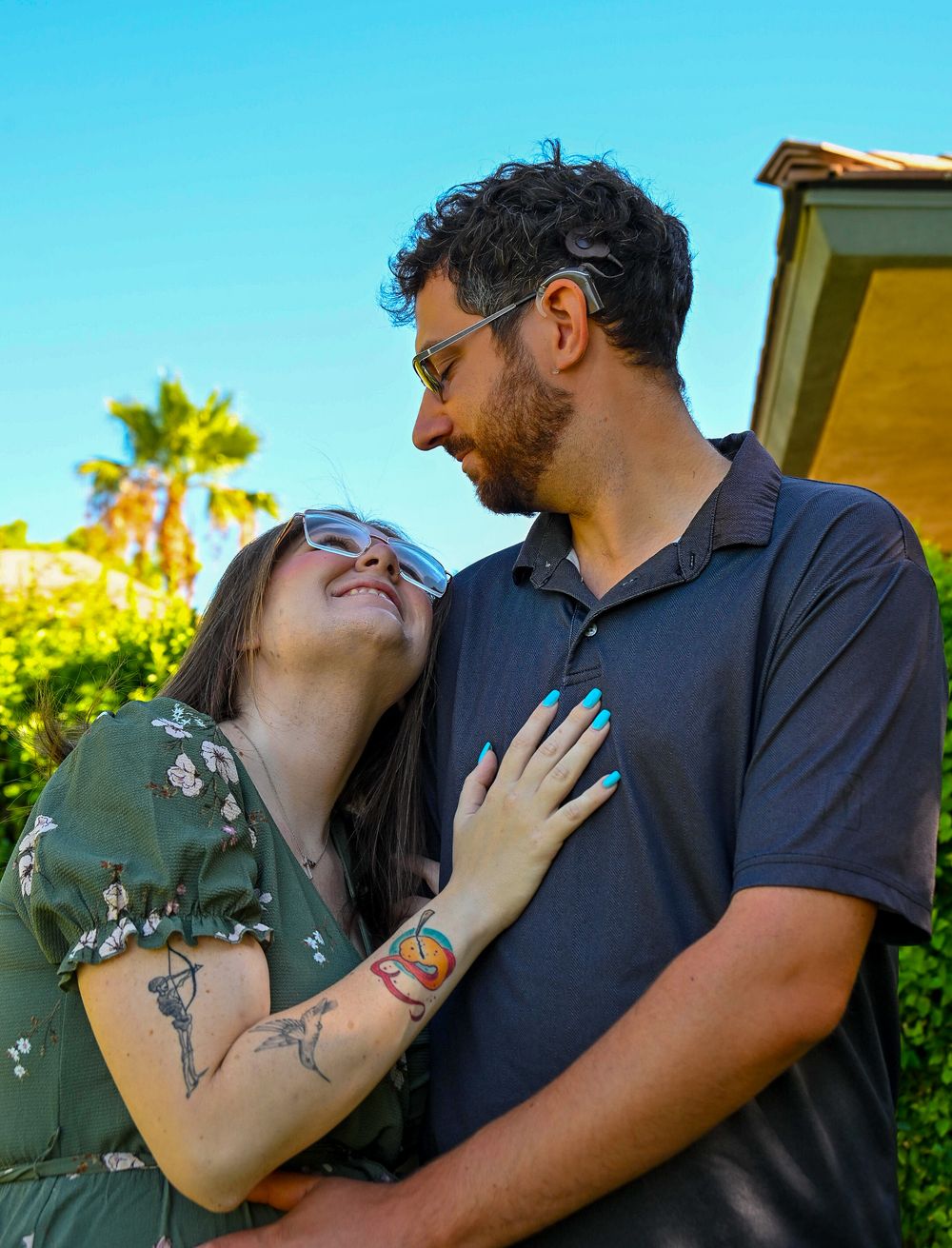 Happy pregnant couple embracing and smiling at each other outdoors in sunny garden setting.