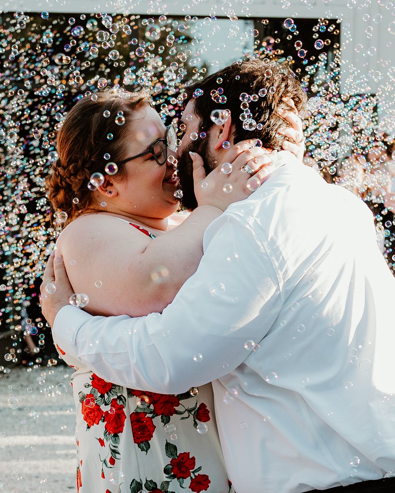 Two people embrace in white outfits with red roses and confetti floating around them.
