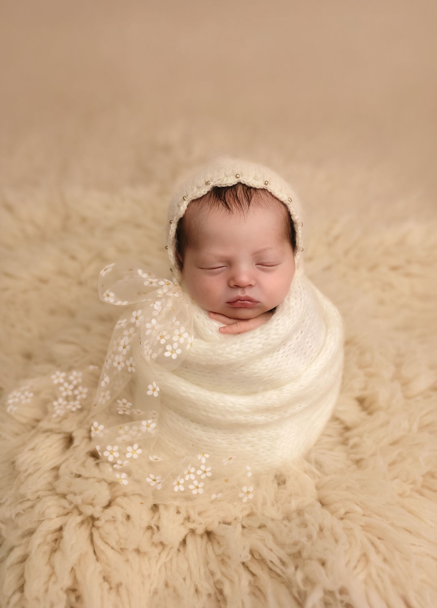Newborn baby girl in soft white wrap and lace bonnet on white flokati rug at Charlottesville photography studio.