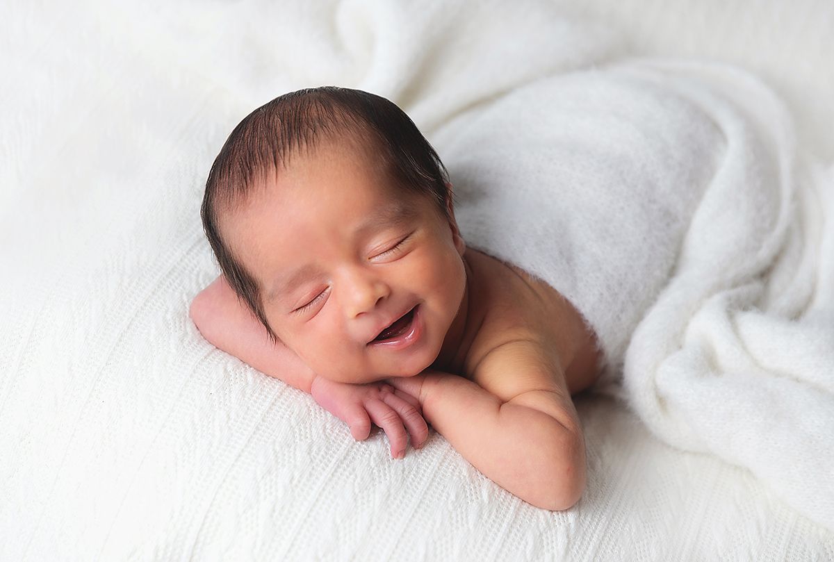Newborn baby smiling while sleeping peacefully on soft white blankets during professional photo session. During a newborn session in London