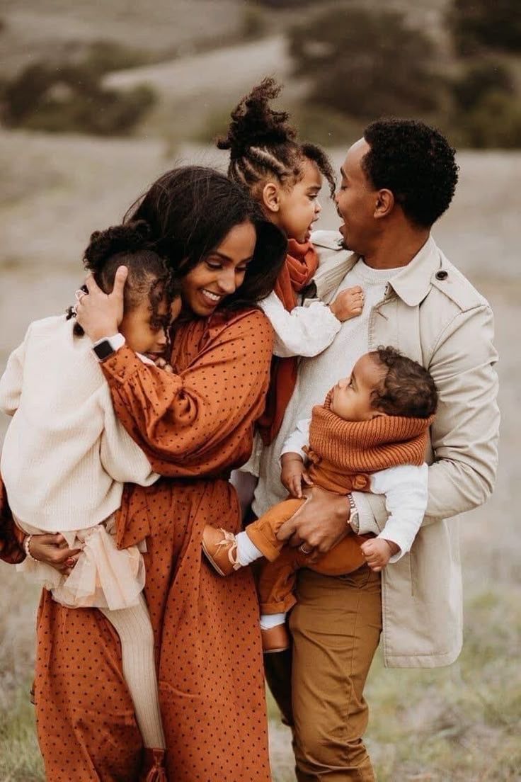 A family of four wearing warm earth tones embraces while standing outdoors during a lifestyle portrait session.