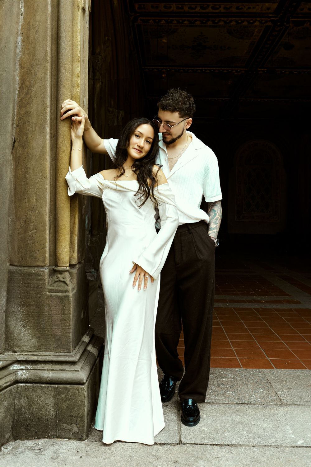 Romantic engagement photo of couple in white outfits against stone archway.