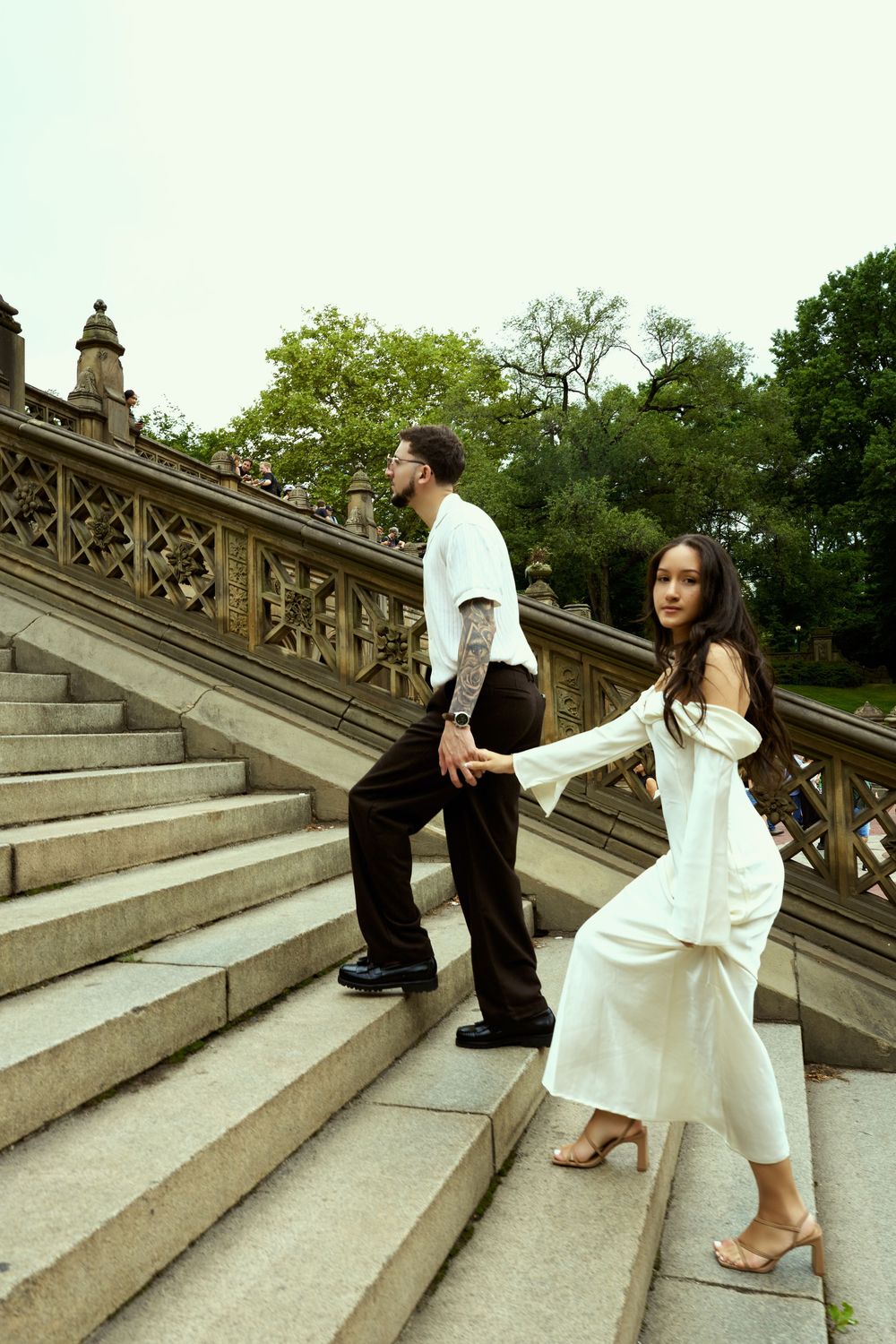 Couple in coordinated white outfits ascending grand stone staircase.