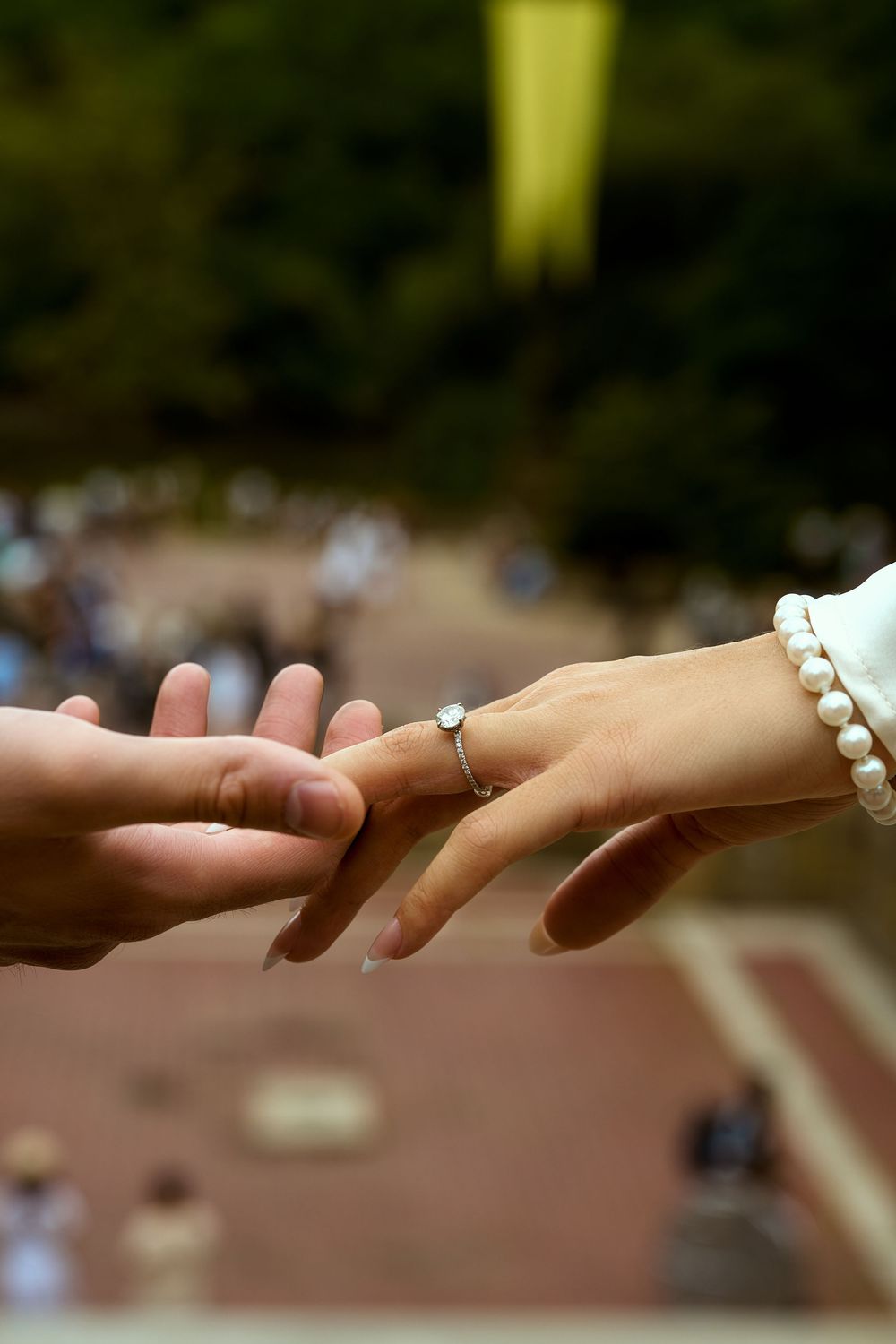 A close-up photo of hands during a proposal moment with a pearl bracelet and engagement ring.