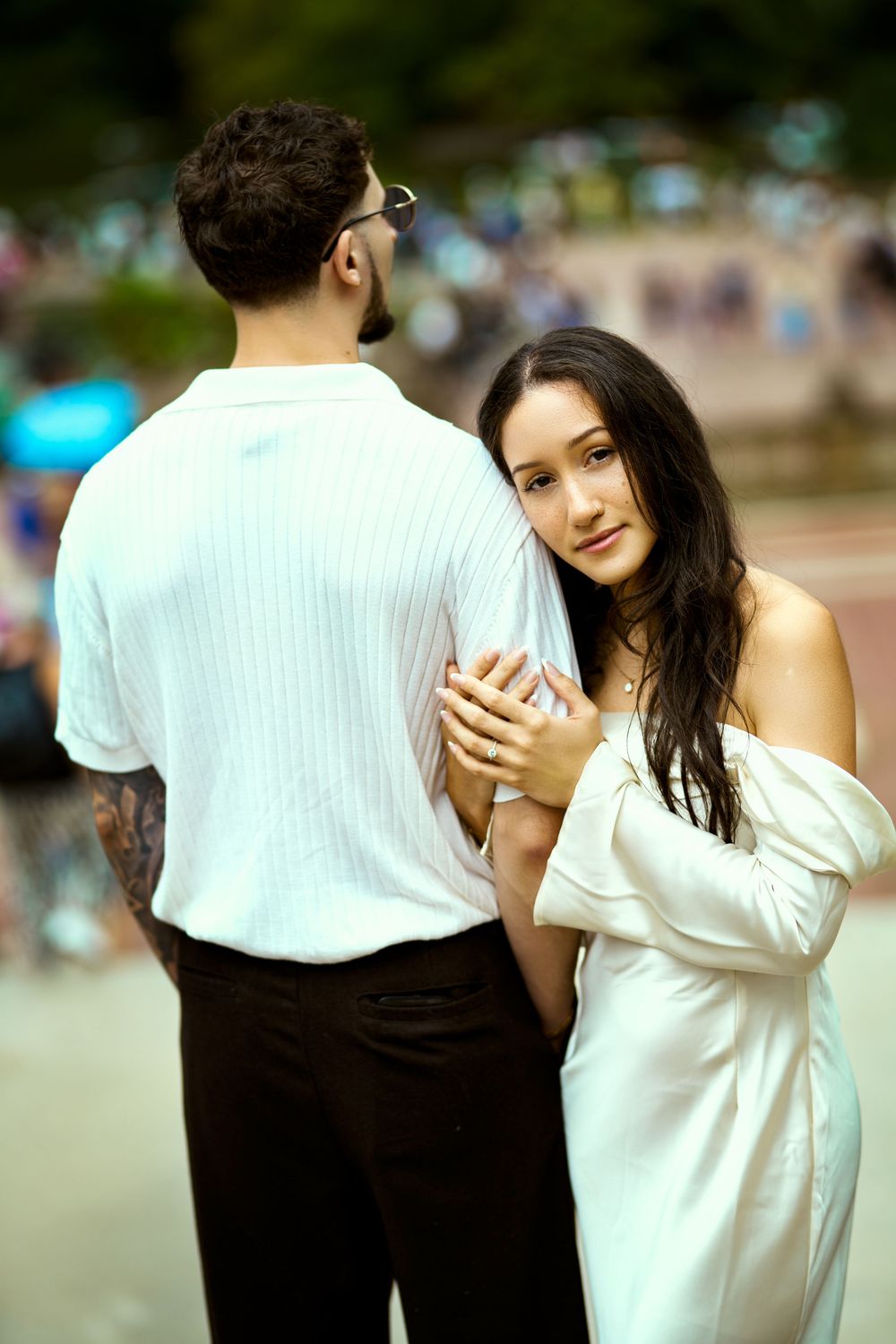 A couple in coordinated white and black outfits poses playfully in an outdoor setting.