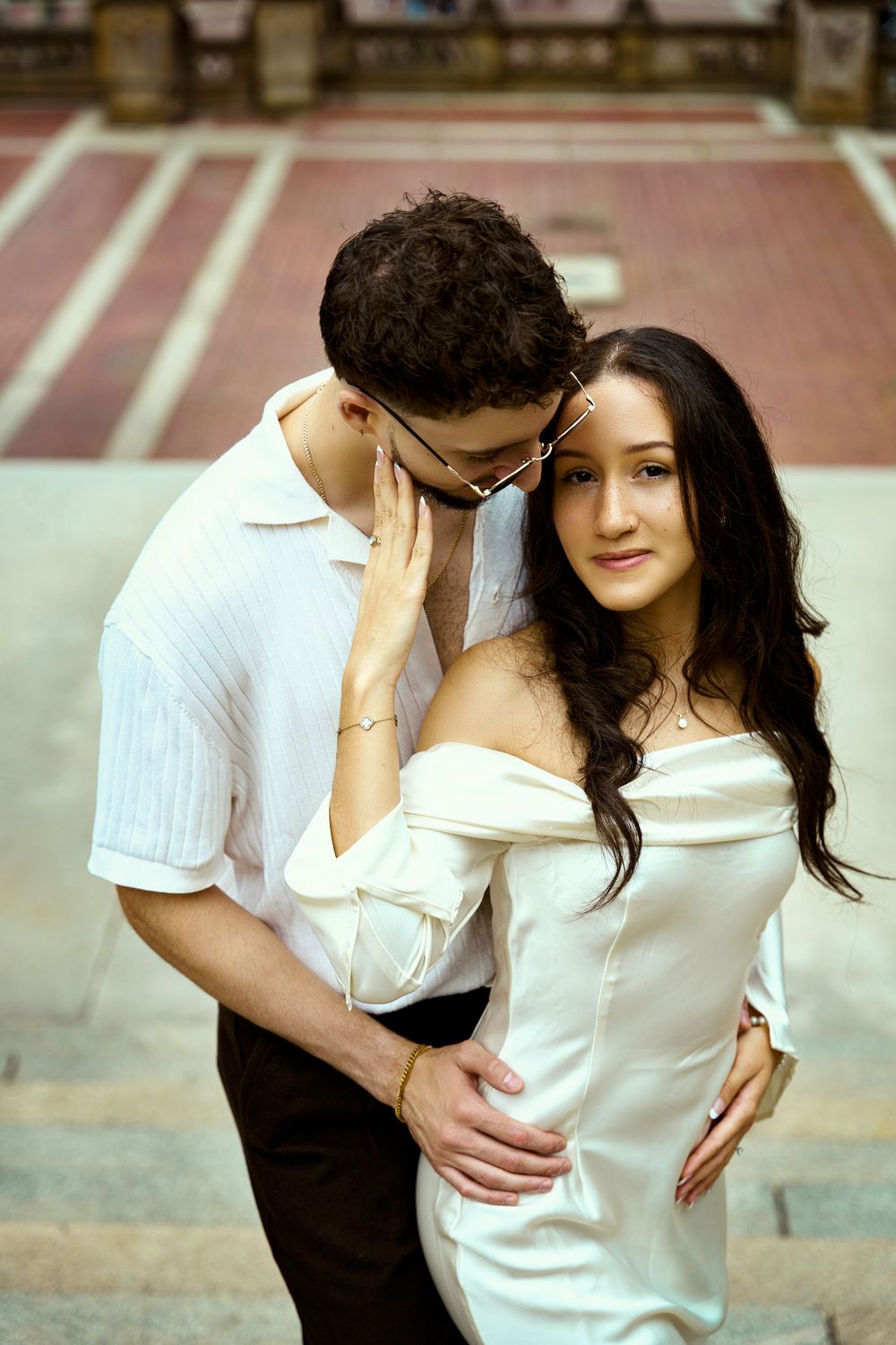 A tender romantic moment between a couple wearing matching white outfits on stone steps.