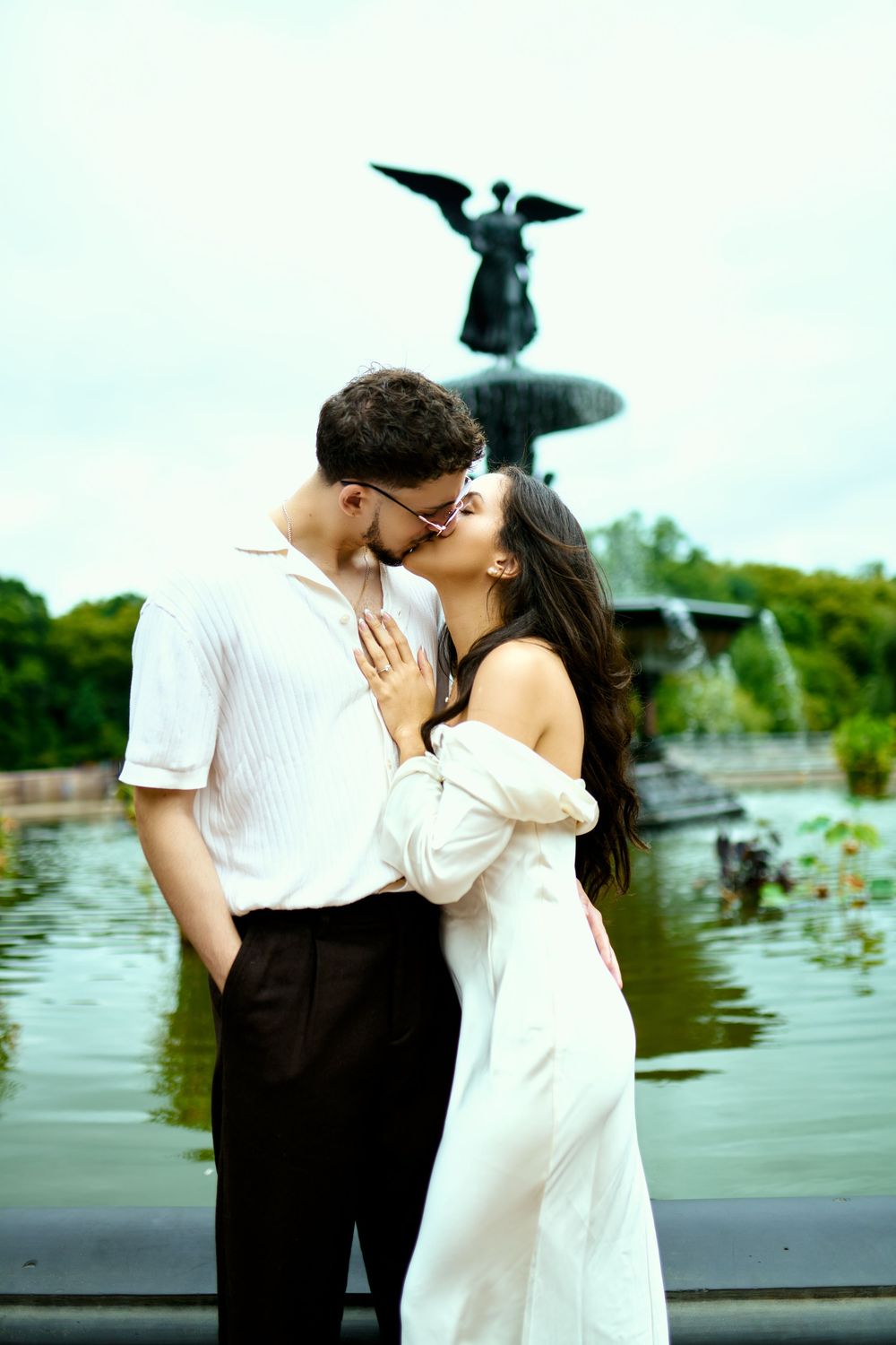 A couple shares a kiss in front of the iconic Bethesda Fountain angel statue.
