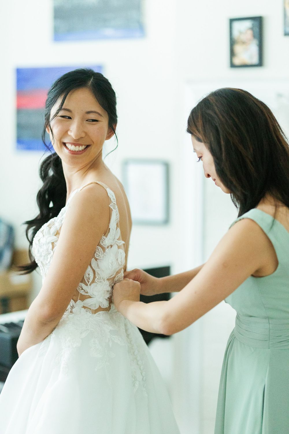 A joyful moment during wedding dress fitting as the bridesmaid helps adjust the beautiful lace gown.