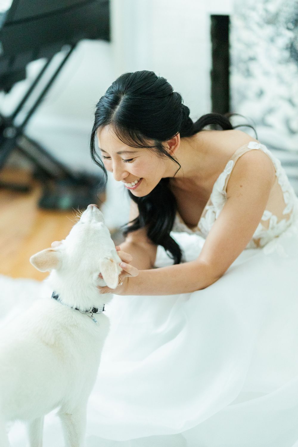 A woman in a white dress shares a tender moment with her white dog in an indoor setting.