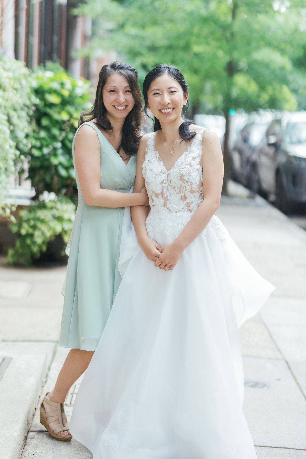 Bridesmaids in mint green dresses pose with the bride in a white lace wedding gown on a sidewalk.