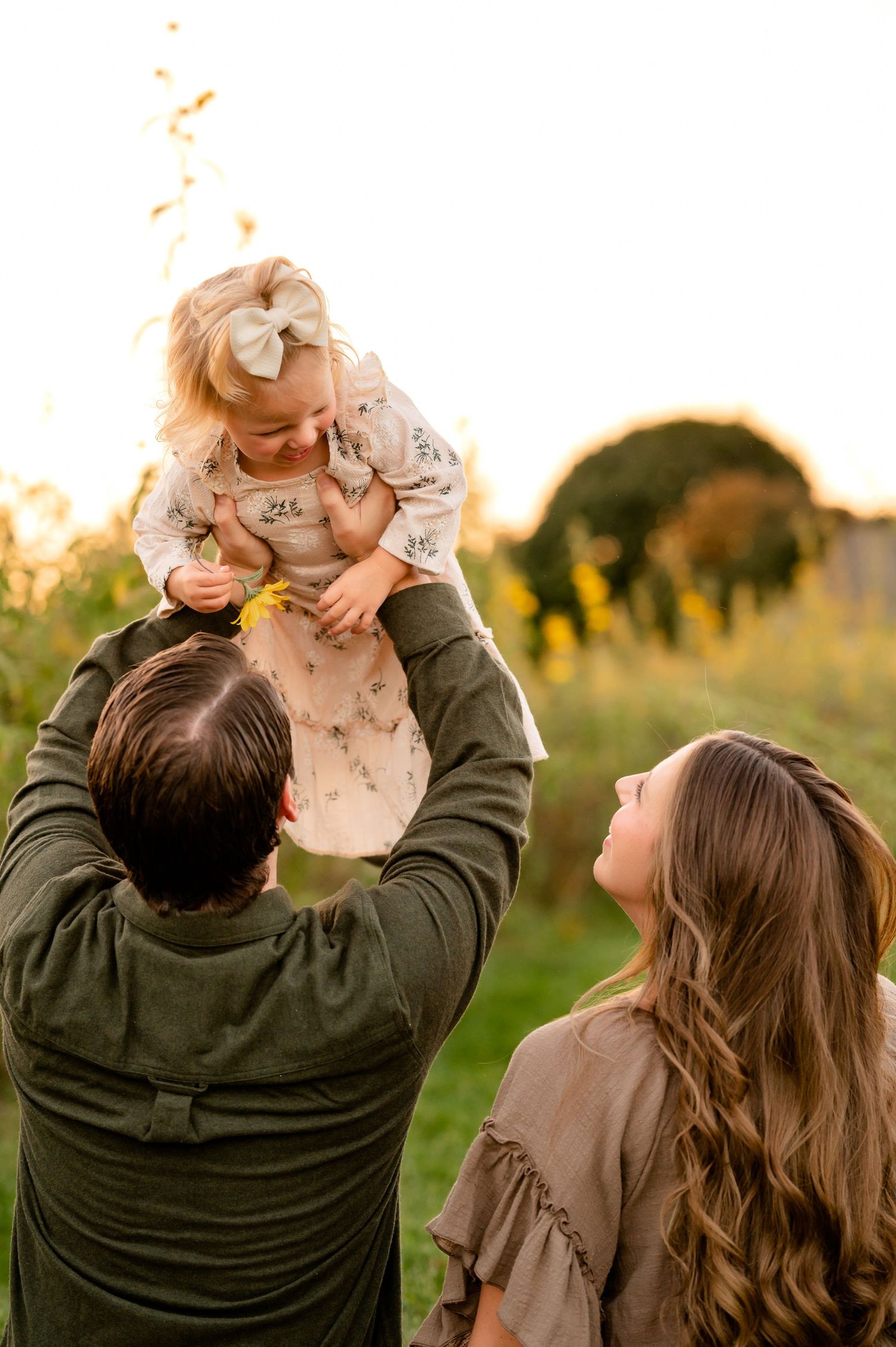 A joyful outdoor family scene with a child being lifted up against the sunset created by Storms Photography in Pennsylvania.