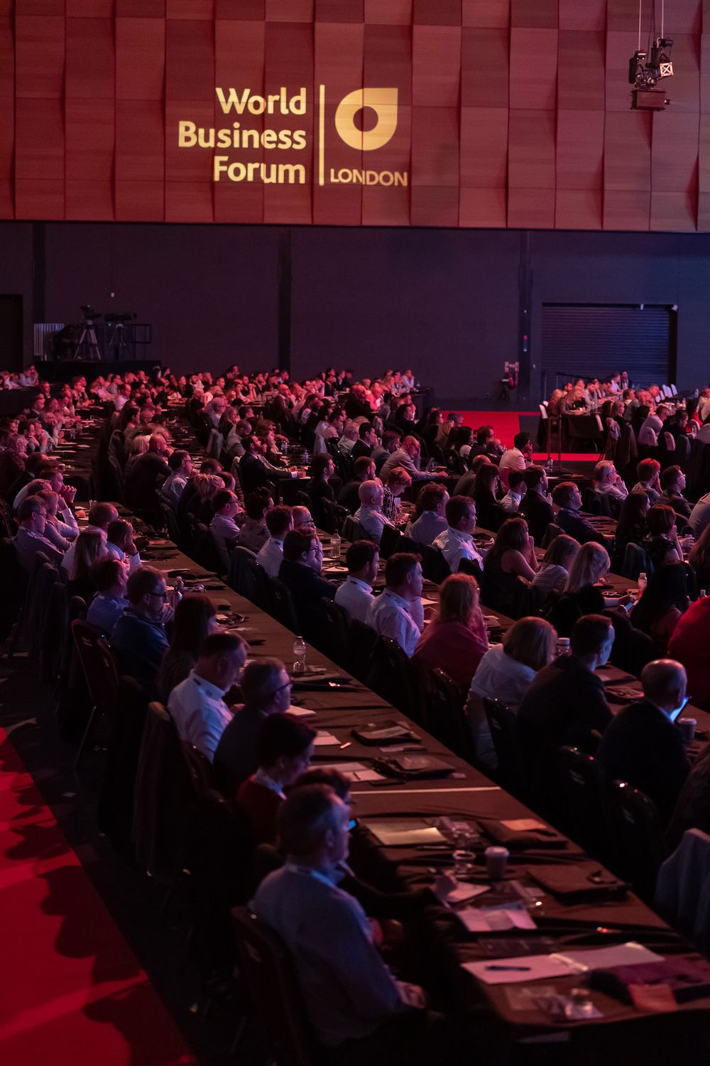 Large audience seated in rows at the World Business Forum London event with red lighting and stage visible.