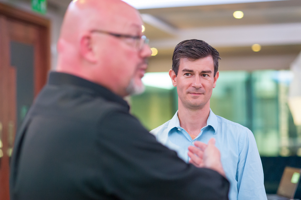 Two people engaged in conversation in an office environment with blurred background lighting.