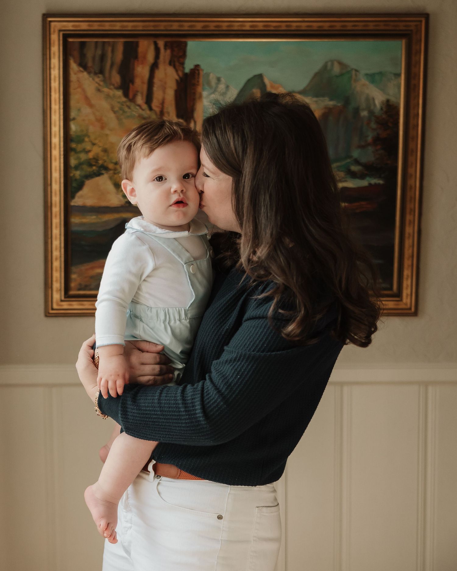 A tender moment captured in a living room with framed landscape paintings on the wall in natural lighting.