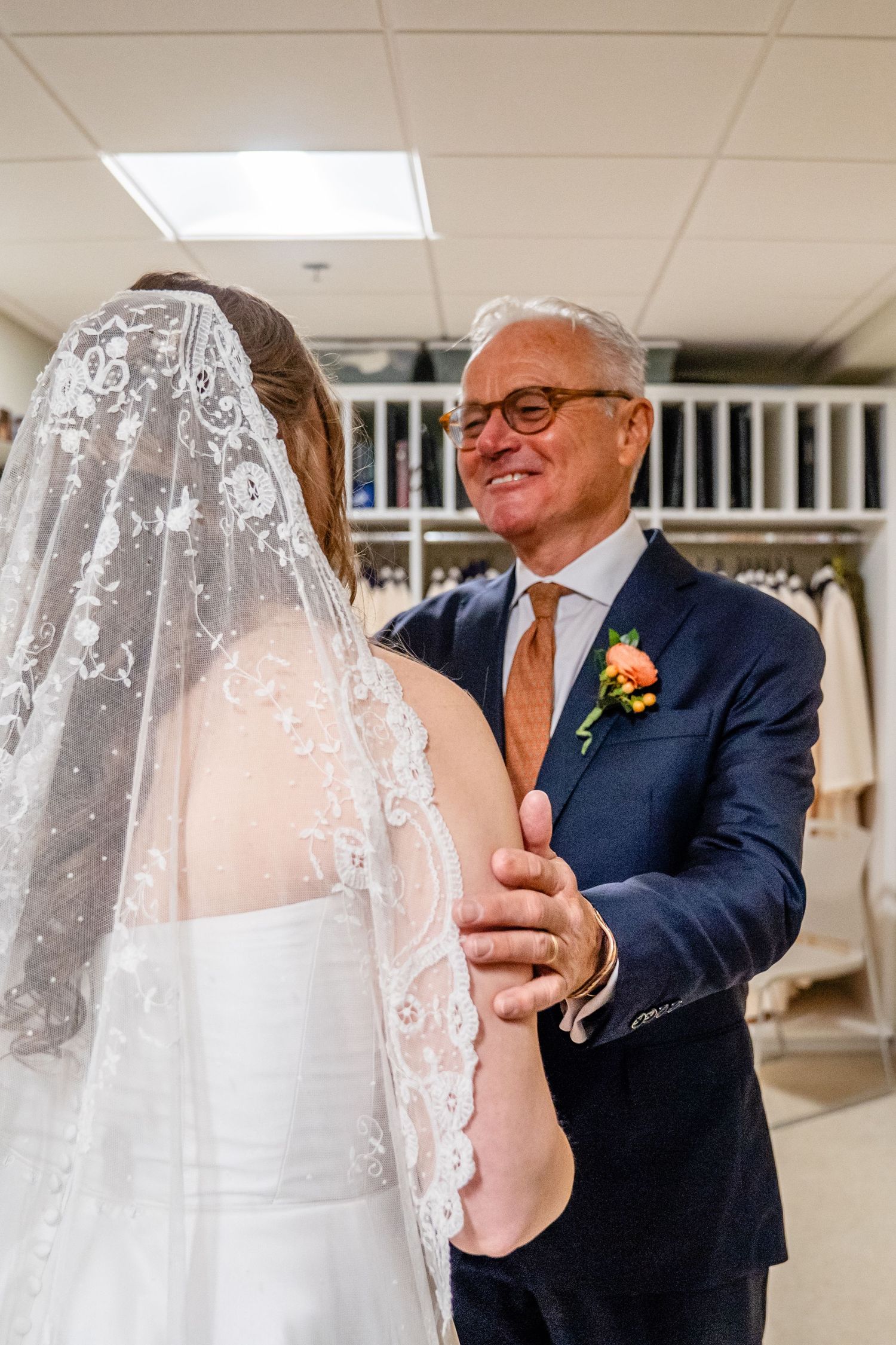 A tender moment captured during a wedding ceremony with a bride in a lace veil and her companion in a navy suit.