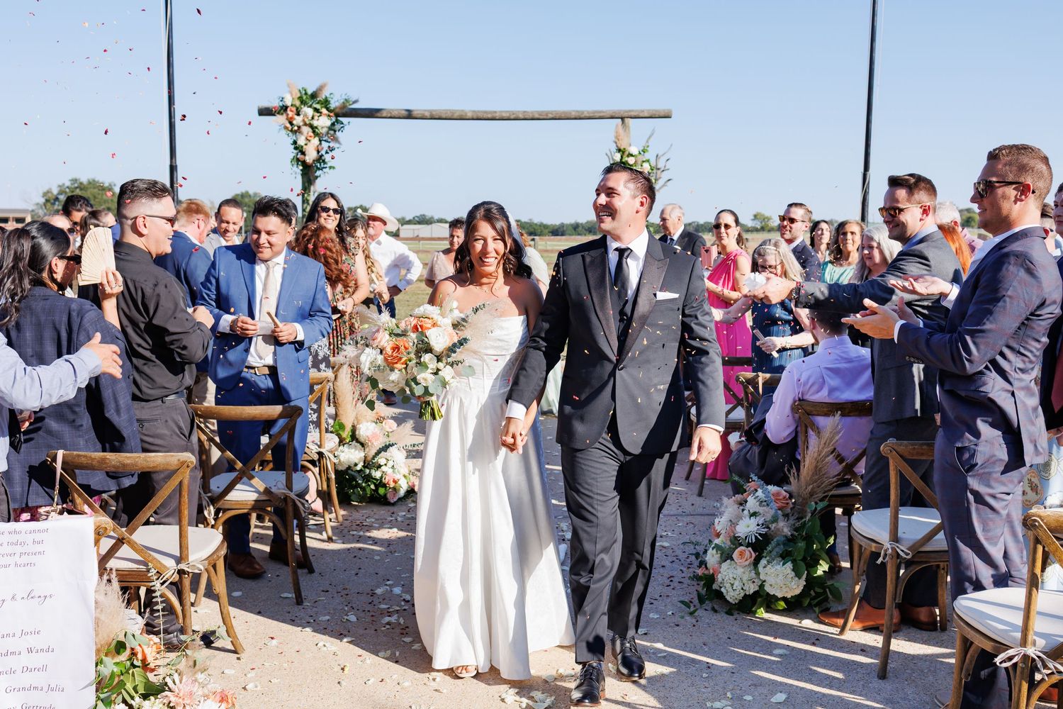 A bride and groom poses together in a romantic Dallas garden wedding venue decorated with pink and red flowers and greenery along a railing.