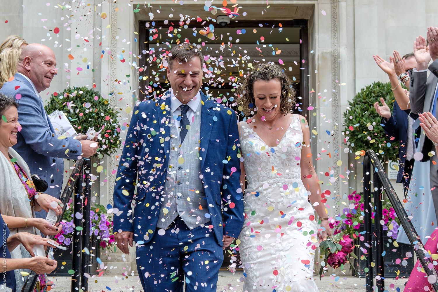 Confetti rains down on a newlywed couple exiting a church as guests celebrate at their wedding ceremony.