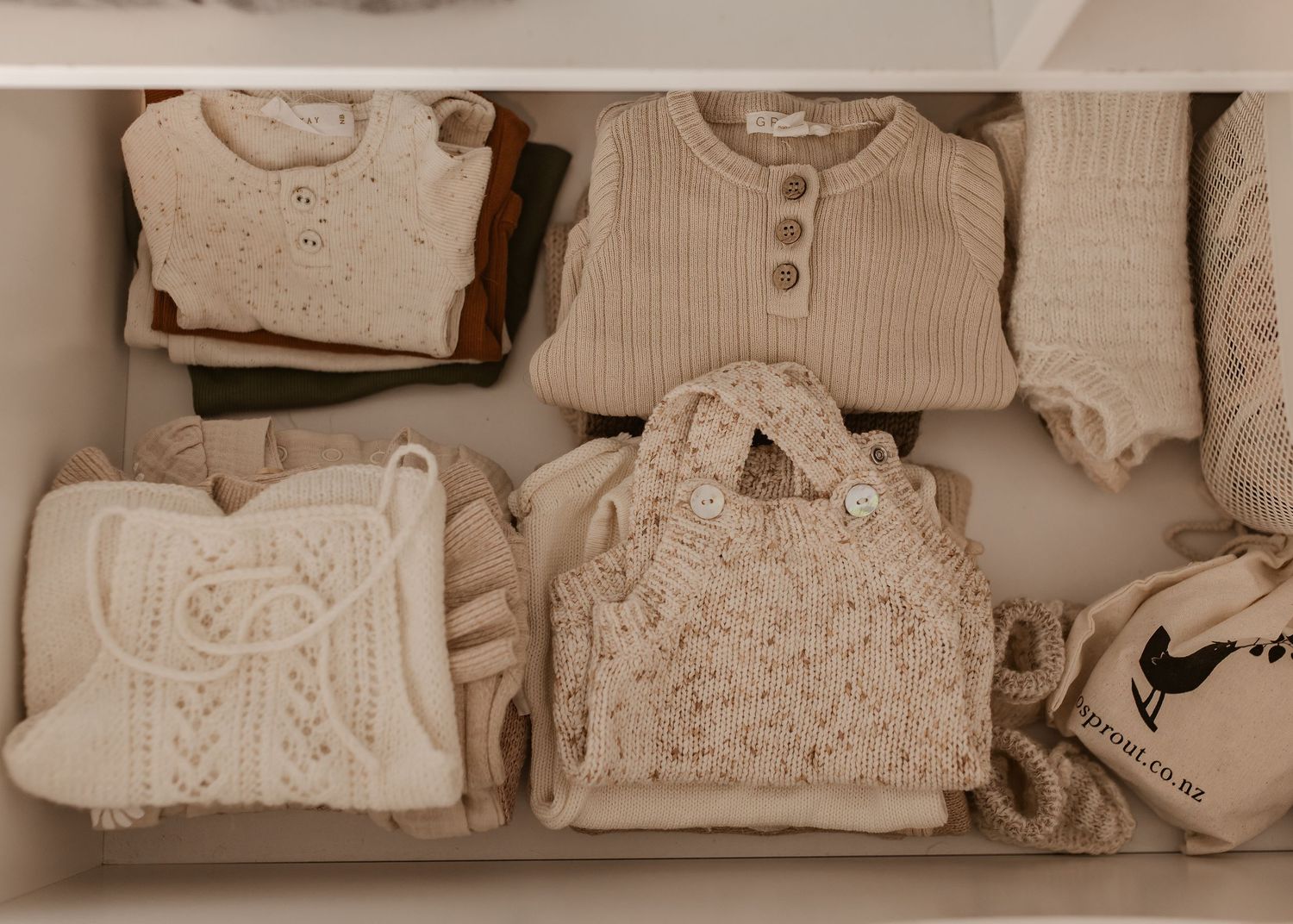 Neatly folded cream and beige knit sweaters and winter clothing arranged on closet shelves.