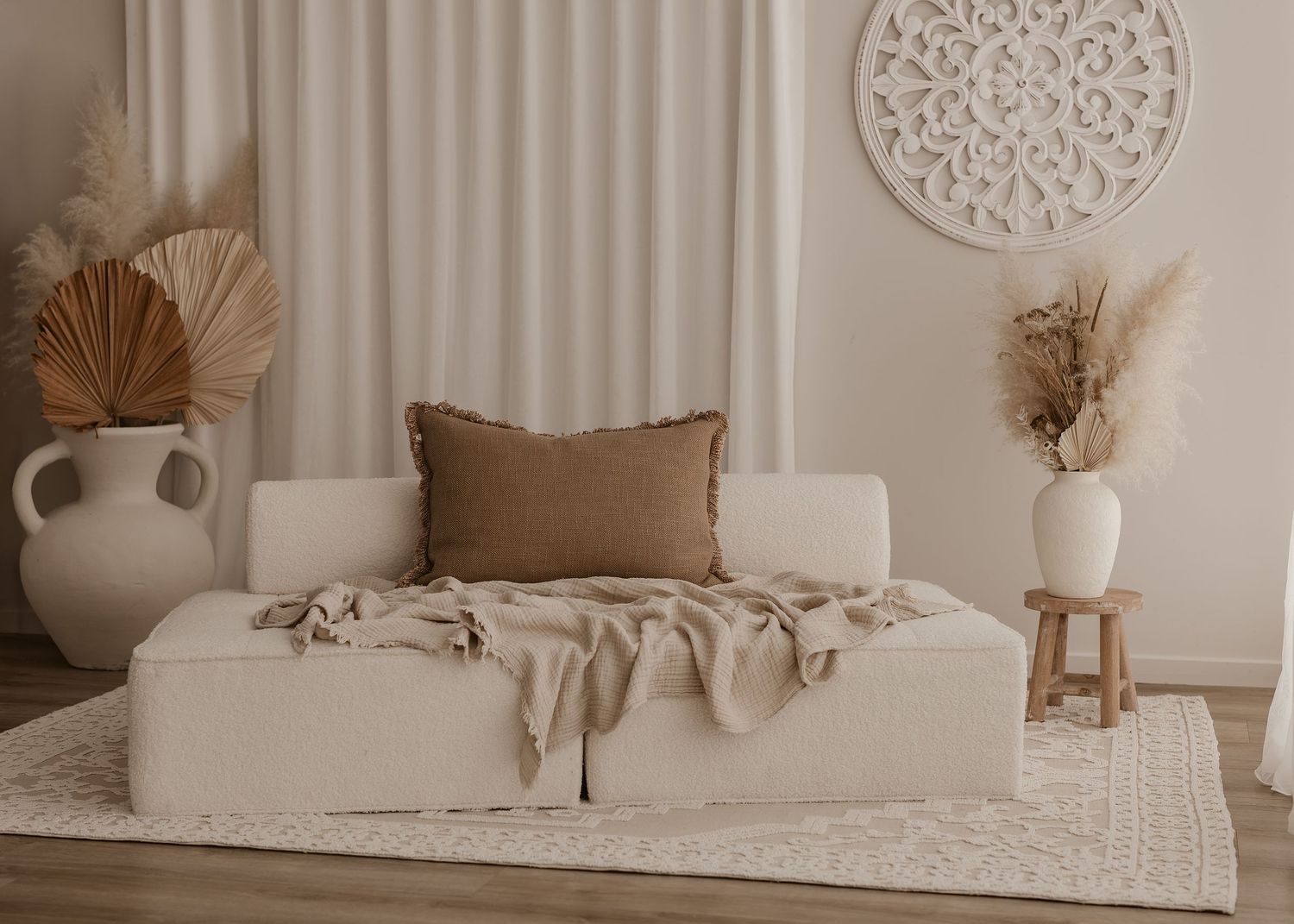 Minimalist cream-colored living room with couch, decorative vases, pampas grass, and circular wall art in neutral tones.