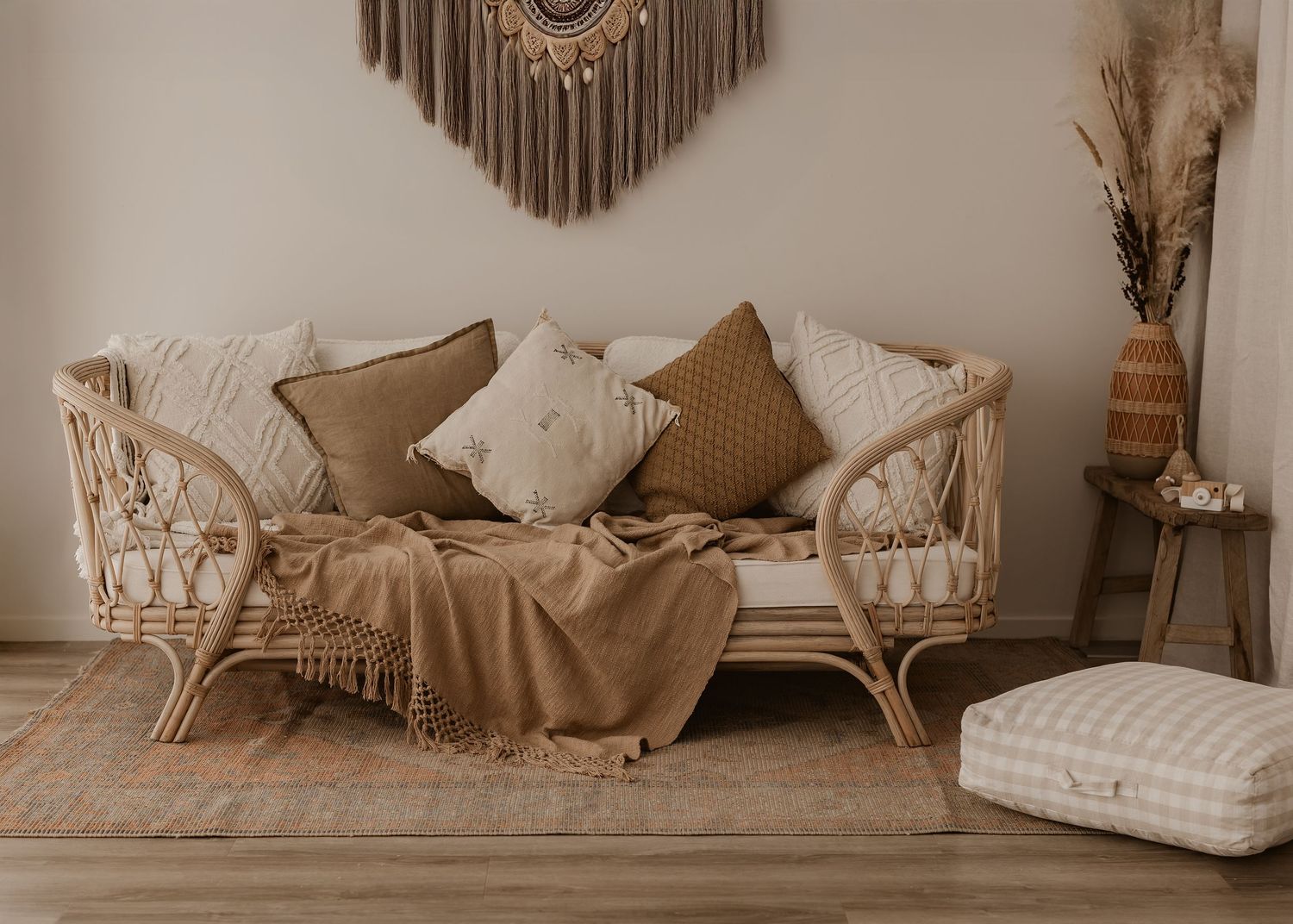 Boho rattan couch with beige cushions and throw decorated with macrame wall hanging and pampas grass in corner.