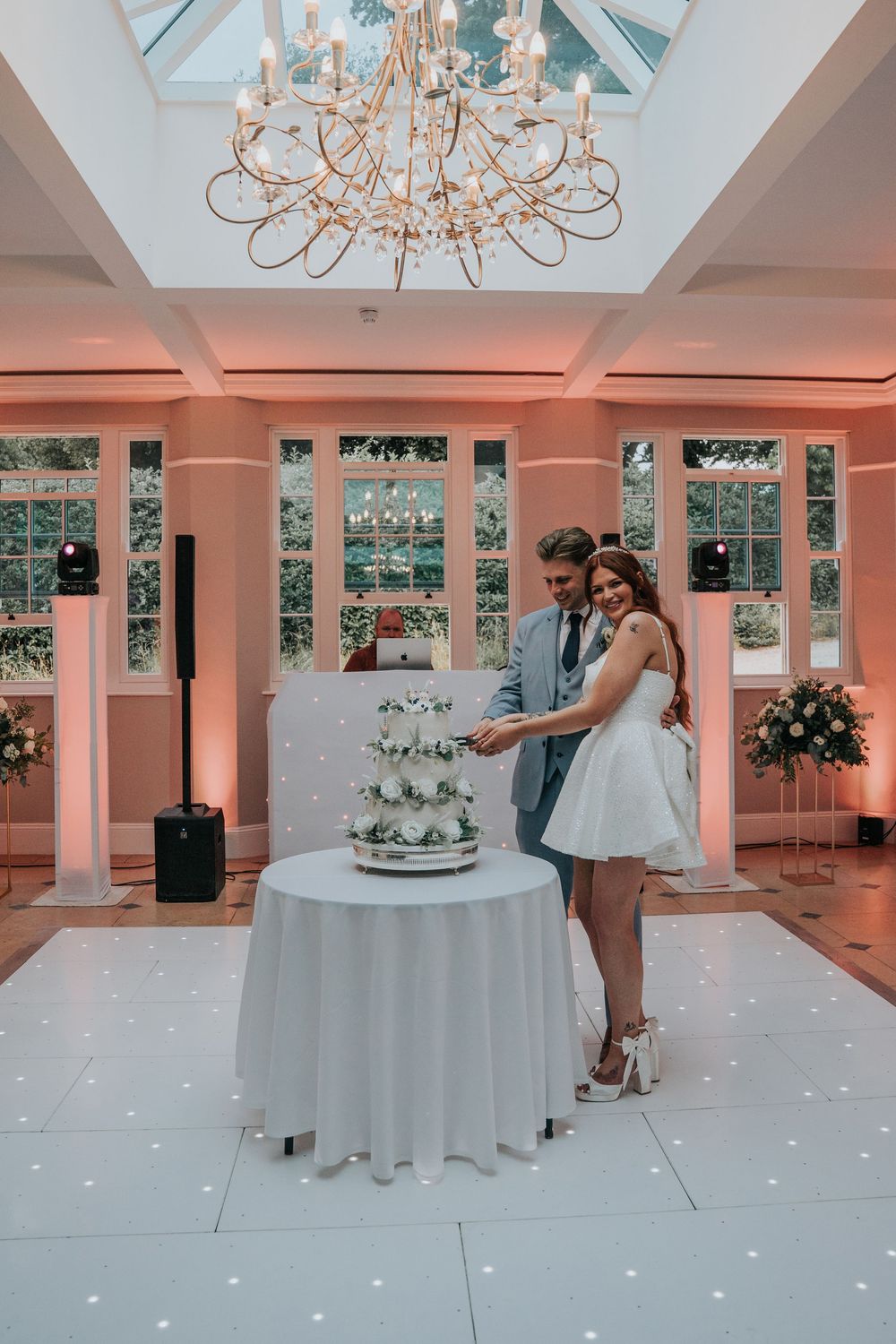 Newlyweds cutting cake at Rockbeare Manor reception under chandelier