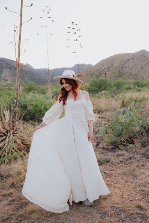 A flowing white dress dances in the wind against desert mountains and cacti.