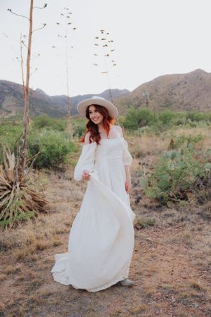 A romantic desert photoshoot features a flowing white dress and wide-brimmed hat.