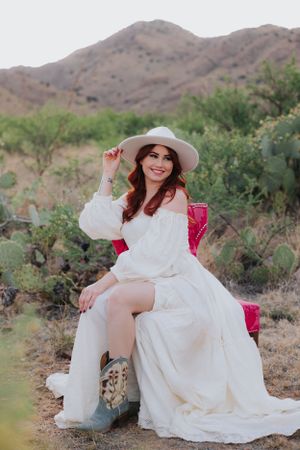 A dreamy desert scene with a white dress, pink chair, and mountain backdrop.