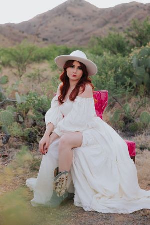 An elegant desert portrait featuring a white dress and vintage-style pink chair.