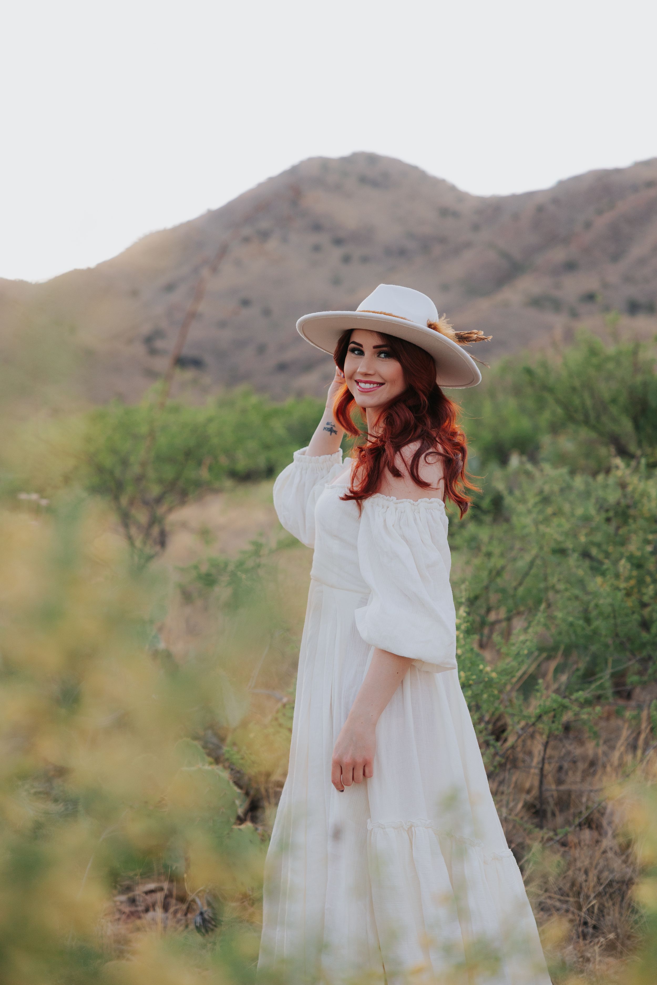 A flowing white dress twirls gracefully against a desert mountain backdrop with desert flora.