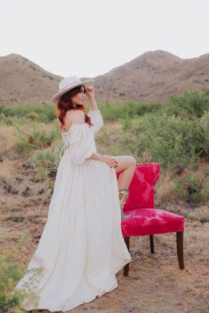 Ethereal desert photoshoot featuring white dress and magenta accent chair among desert brush.