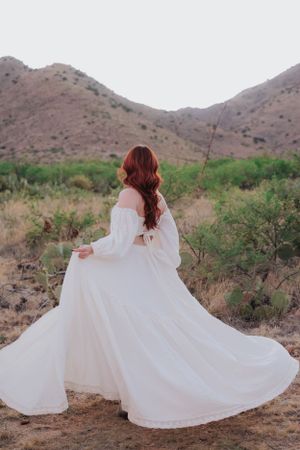 White dress twirls dramatically against desert mountain backdrop during sunset photoshoot.