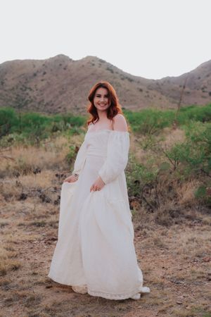 Dreamy desert portrait session with off-shoulder white dress and mountain scenery.
