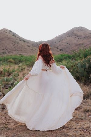 Elegant white dress flows in desert breeze with mountains in background.