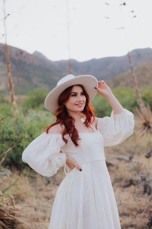 A sun hat and white dress create an elegant silhouette against rugged mountain scenery.