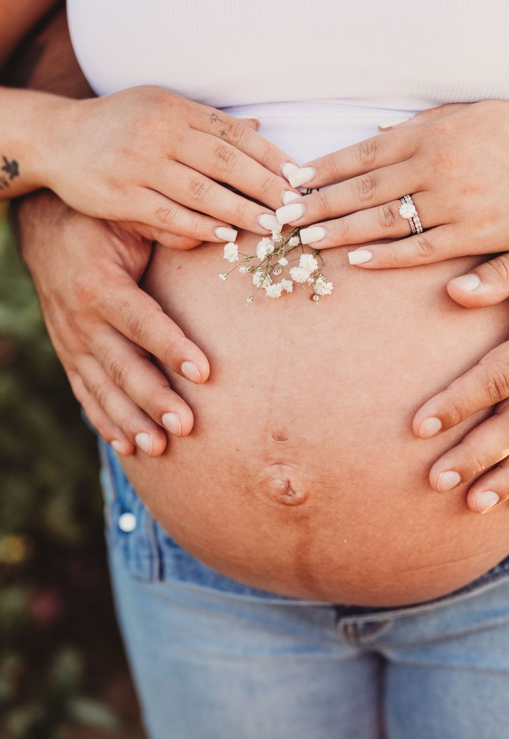 Five progression shots showing a pregnant belly with delicate white flowers placed against bare skin and denim.
