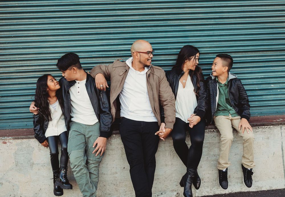 People dressed in casual clothing lean against a white wall while engaging in animated conversation together.